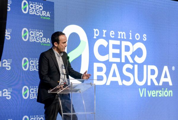 Persona en traje oscuro habla desde un podio transparente durante los Premios Cero Basura VI versión, con una gran pantalla azul de fondo que muestra el logo del evento.